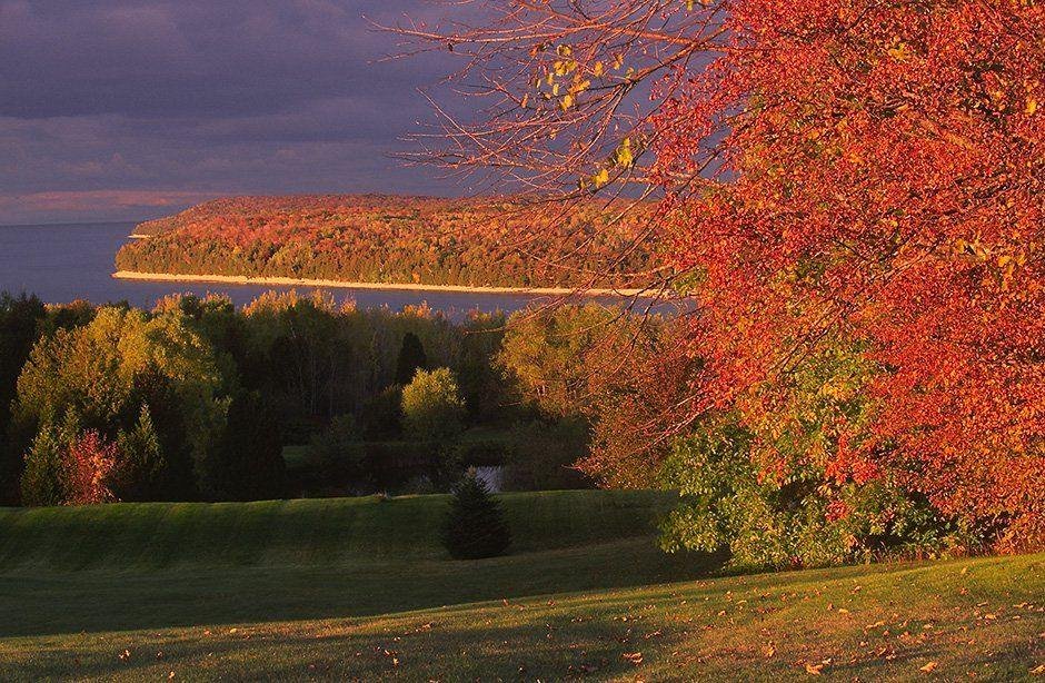 Grandview Overlook rests atop the Niagara Escarpment bluffs of Ellison Bay, Wisconsin looking northward. The scarlet and bittersweet autumn foliage is interspersed with Brunswick-green cedar trees. The foliage, Kelly-green slopes and golden shorelines all provide a spectacular contrast against backdrops of darkening periwinklepink skies and the ultramarine waters of Green Bay near sunset.