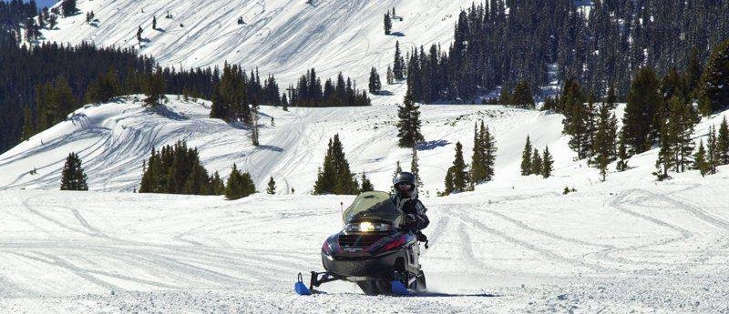 Powder flies as a snowmobiler takes a turn in the snow at Grand Lake near the Colorado River Headwaters Scenic Byway.