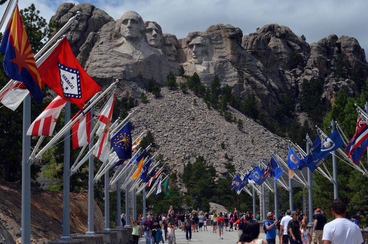 Visitors walking along the Avenue of Flags with Mount Rushmore in the background.