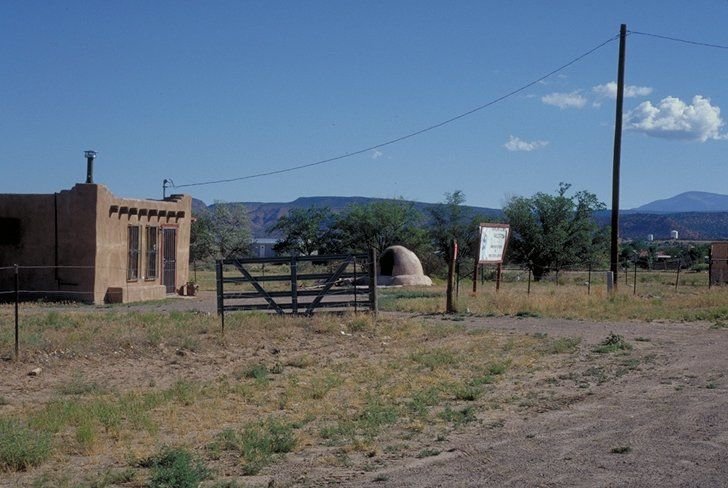 A dome shaped bread oven sits in the front yard of a small brick home.