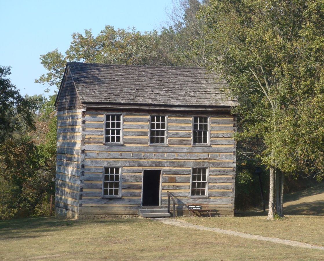 The Lincoln Homestead Cabin stands proudly among the Kentucky landscape, trees casting shadows on its wooden frame.