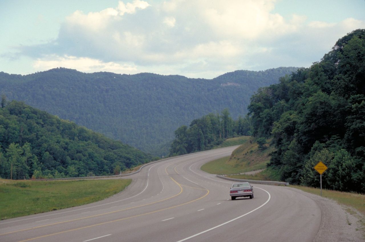A lone driver approaches a curve through tree-covered, rounded mountains on Highway 23, the Country Music Highway, near Pikeville, Kentucky.