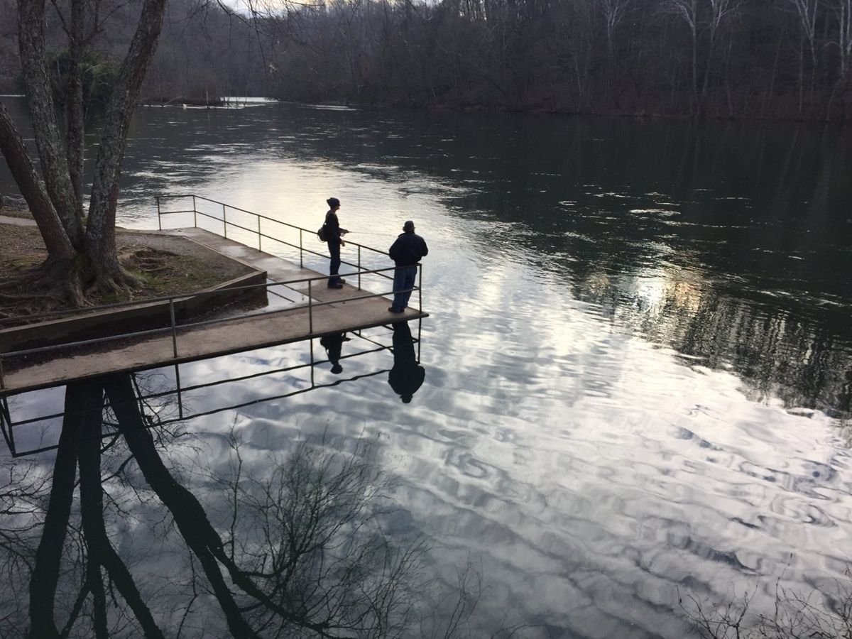 Here a woman with her fishing rod in hand and her friend are at Clear Creek. The concrete platform there offers a good spot to cast a line into the Clinch River. A lovely reflection of the winter hardwoods can be seen in the water.